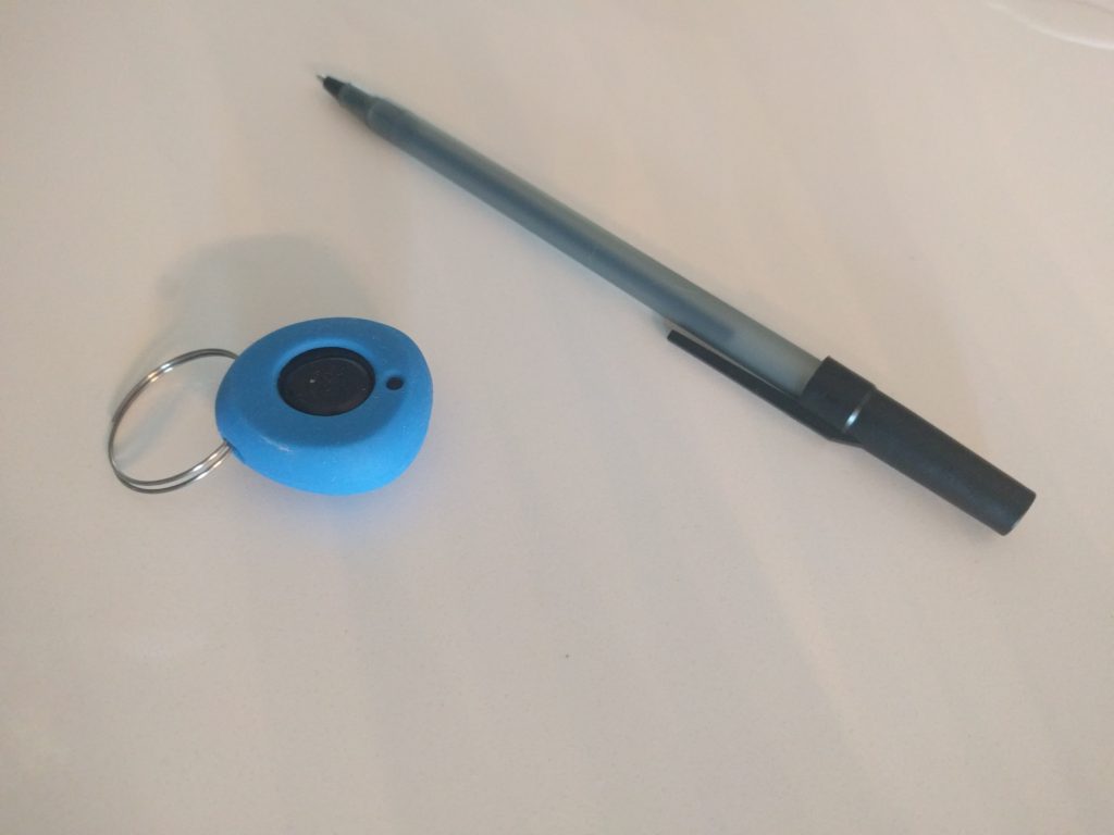 The Pebblebee Stone next to a pen. The other side is covered in the soft plastic.